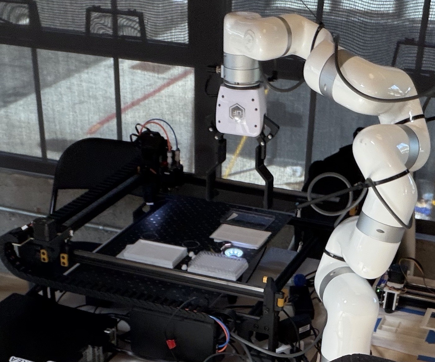 Collaborative robot arm positioned over the BugPicker bed, plates staged below